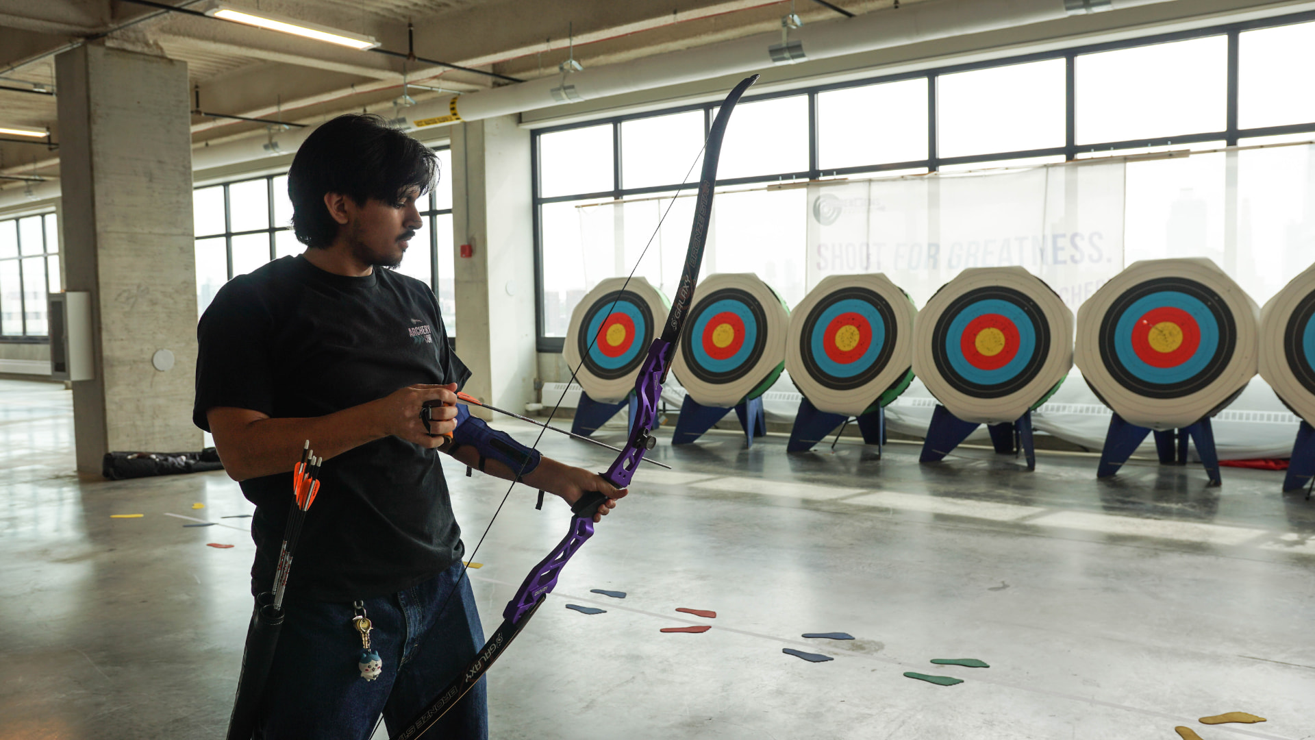 An adult archer preparing to shoot on an indoor range